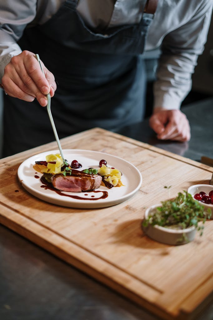 Chef meticulously plates a gourmet dish on a wooden board in a professional kitchen setting.