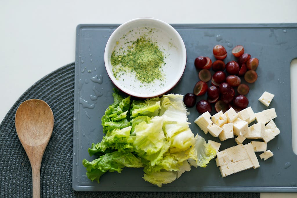 Fresh lettuce, grapes, and tofu with seasoning on a cutting board for a healthy meal preparation.