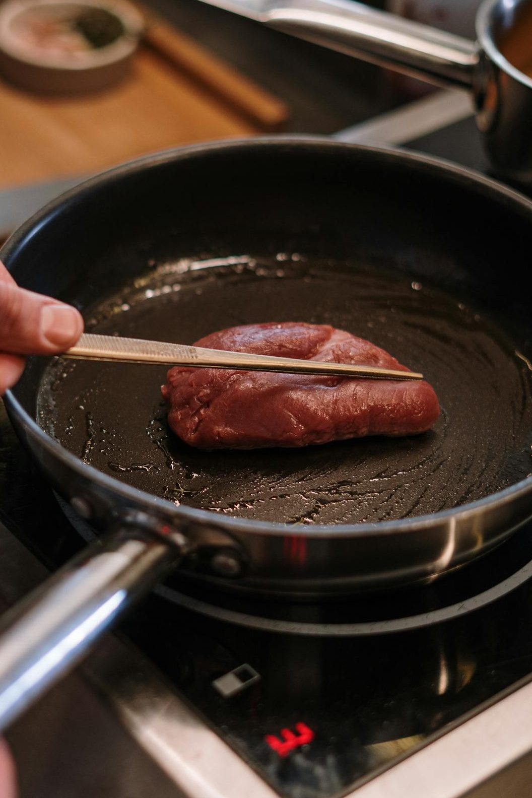 Hands of a chef cooking steak on a stove in an indoor kitchen setting. Close-up view.