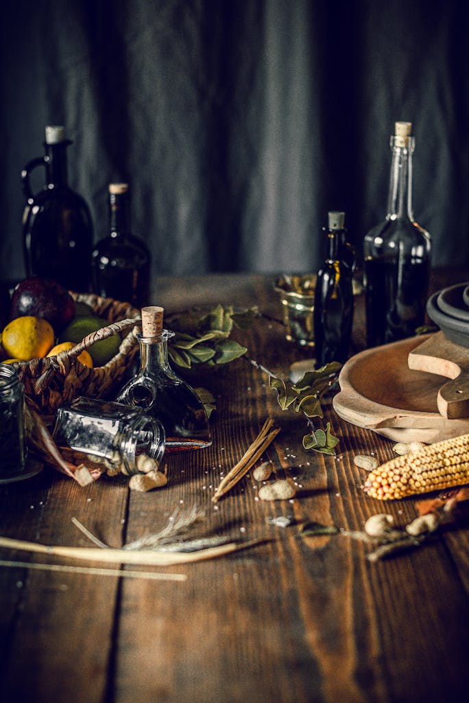 From above of bottles with assorted oil and vinegar placed on wooden table in kitchen near fruit basket composed with corn and herbs