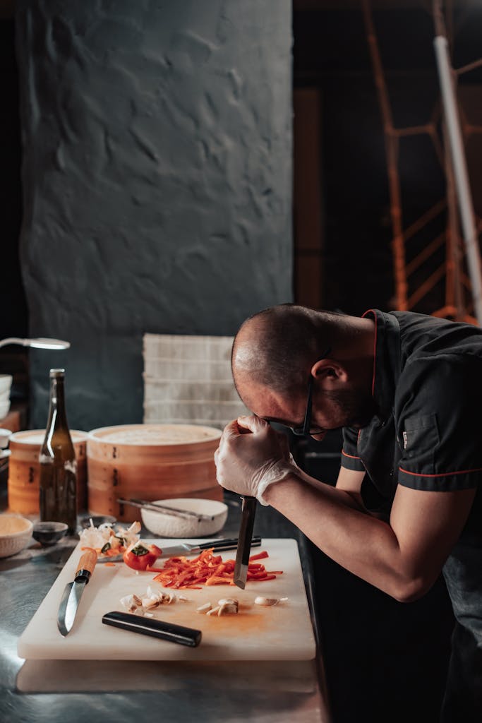 A weary chef leans on a cutting board amidst ingredients in a kitchen setting.