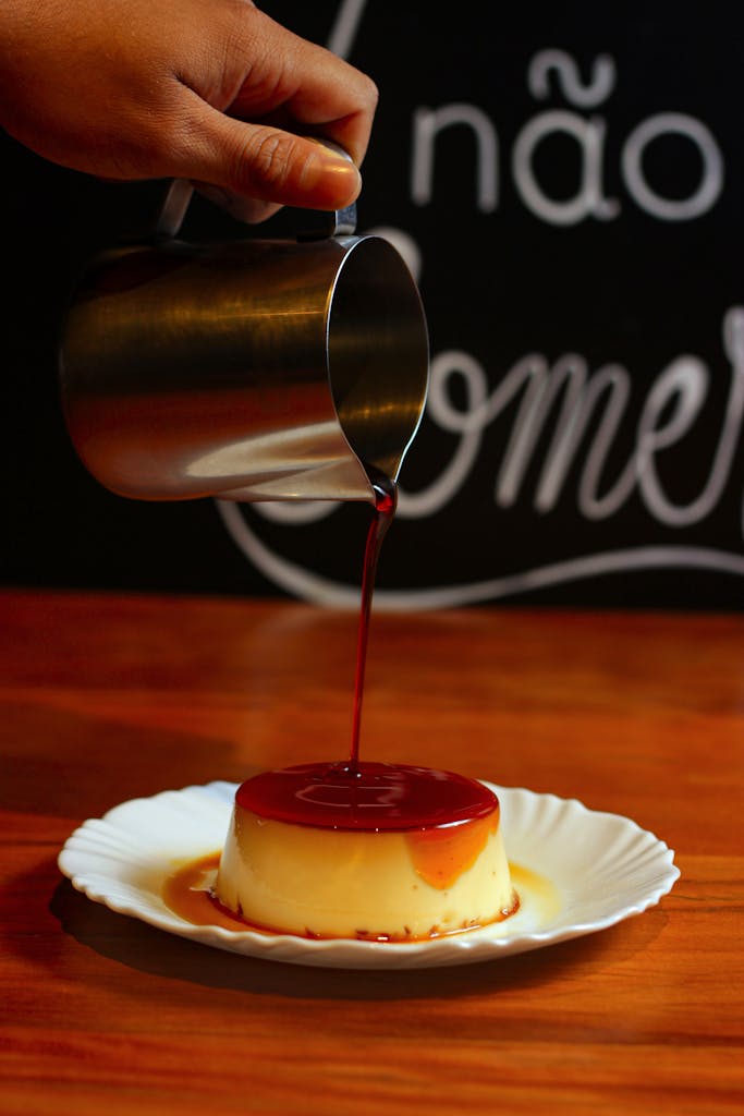Hand pouring caramel sauce over a flan on a plate; close-up view, perfect for dessert presentations.